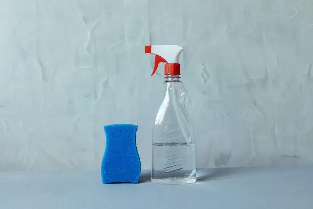Bouteille avec pulvérisateur remplie de vinaigre ménager, près d'une éponge de nettoyage